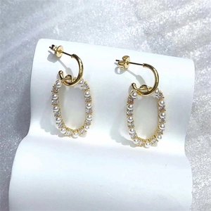 Orecchini geometrici placcati in oro con perle e zirconi su un supporto espositivo bianco