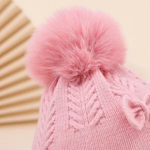 Detailed texture of pink knit baby hat with soft faux fur pompom and woven bow