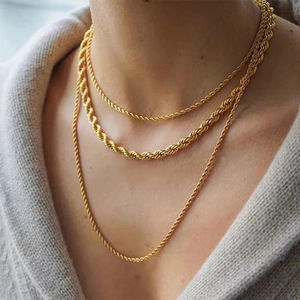 Detailed close-up of layered gold chunky twist rope chain necklaces on a grey knit sweater