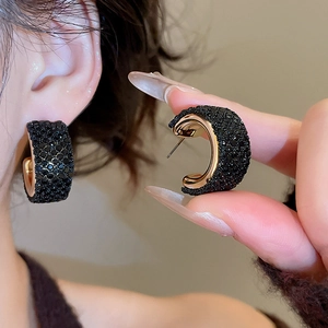 Close-up of C-shaped earrings with black crystals and gold-tone metal finish