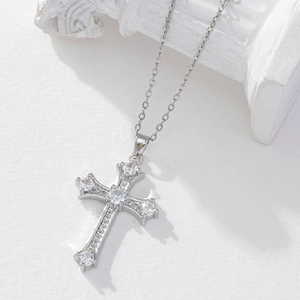 Detail of silver cross necklace with clear zircon stones on a white stone background