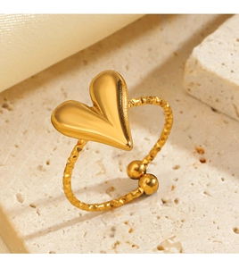 Macro detail of golden heart ring with textured band on a marble stone surface