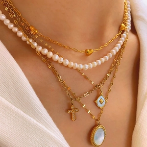 Layered gold necklace set with pearls, cross pendant and shell charm on model