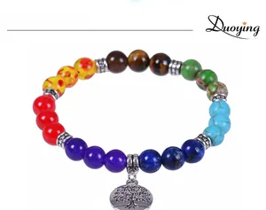 Macro detail of seven chakras beaded bracelet with silver Tree of Life charm on white background