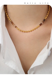 Dettaglio della collana a sfere dorate con pietre marroni su camicia bianca