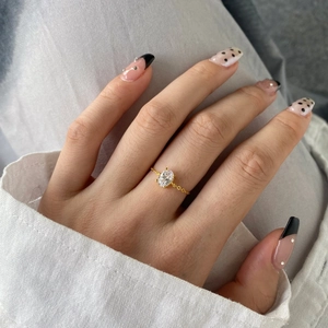 Detail of a gold chain link ring with a clear oval gemstone on a model's finger