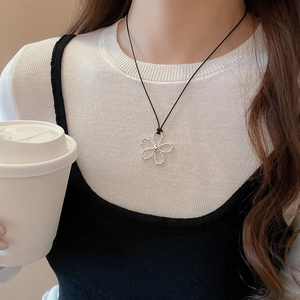Pendentif fleur argenté évidé sur cordon noir porté par un mannequin dans un café chic