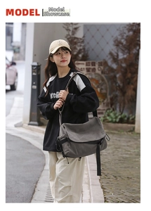 Detail view of large dark grey canvas messenger bag worn in a street fashion style