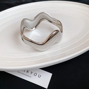 Detailed macro view of an irregular wavy silver bangle featuring a high-polish mirror finish