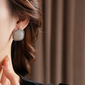 Close-up of a silver square stud earring with sparkling cubic zirconia on a female model