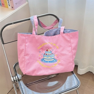 Detail of pink canvas tote bag showing cake embroidery and blue gingham strap