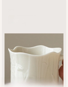 Detail of white ceramic cup with irregular wavy rim and elegant embossed texture