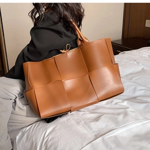Detail of a large brown woven PU leather tote bag displayed on a soft bed