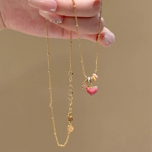 Macro detail of a gold chain necklace with pink enamel heart pendant and colorful beads