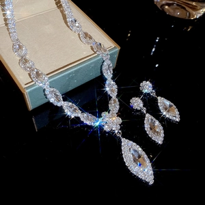 Sparkling silver necklace and earrings set with marquise stones on a black reflective surface