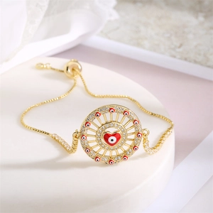 Macro shot of adjustable gold bracelet featuring devil's eye and red heart zircon pendant