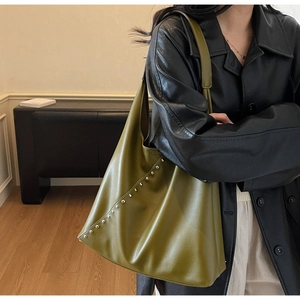 Olive green large faux leather tote bag with silver studs worn by model in minimalist home