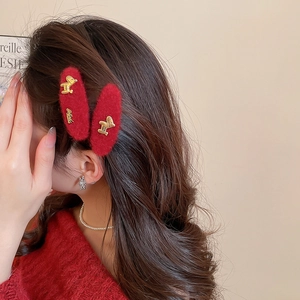 Detail view of two red plush drop hair clips with golden dog charms on a woman's side hair