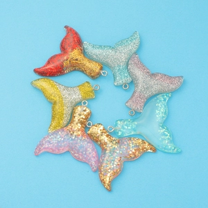 Detail of seven resin mermaid tail pendants with colorful glitter gradient on blue background
