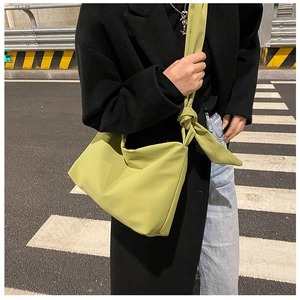 Outdoor street shot of a casual green crossbody bag with a distinctive knot shoulder strap
