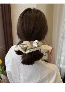 Detail of green plaid lace scrunchie with bear charm on model's low bun hairstyle