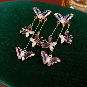Détail de boucles d'oreilles papillon en cristal violet avec pompons dorés élégants