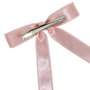 Detail of pink satin bow hair clip featuring scalloped edges and metal alligator back clip