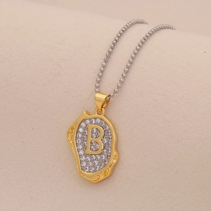 Macro shot of two-tone bead chain with irregular gold pendant and crystal letter B