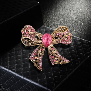 Luxury gold bow brooch featuring pink rhinestones and a teardrop gem on a black box