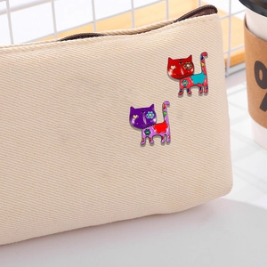 Colorful cartoon cat enamel pins in red and purple pinned on a beige canvas bag