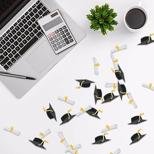 Graduation party confetti set with black caps and white scrolls on office desk