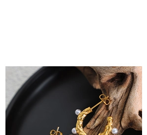 Close-up of golden hammered C-shape earrings with inlaid white pearls on wood