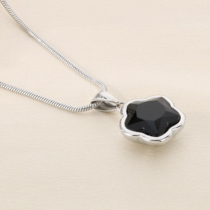 Macro detail of silver snake chain with a black five-petal flower crystal pendant