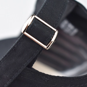 Detailed macro view of the black cotton twill baseball cap with a gold metal strap buckle