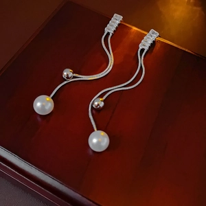 Macro shot of silver pearl tassel earrings with zircon studs on a dark wooden box