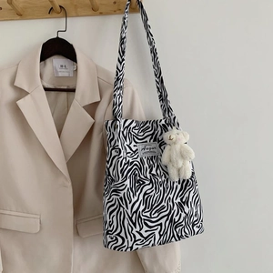 Detail of zebra print canvas tote bag featuring a cute white plush bear charm on a hook