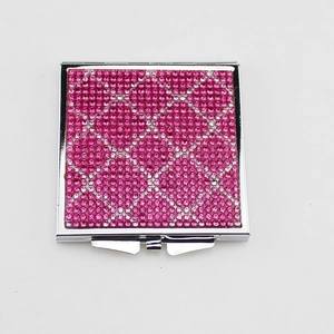 Miroir de maquillage pliable rose orné de strass avec motif mosaïque sur fond blanc épuré