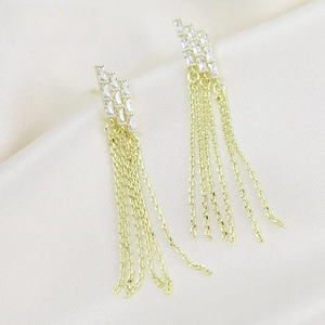 Detalle de pendientes dorados con borlas y circonitas sobre tela de raso crema