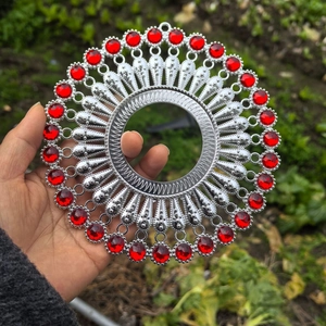 Detailed close-up of a silver sunburst wall decor with a red gemstone center held by hand
