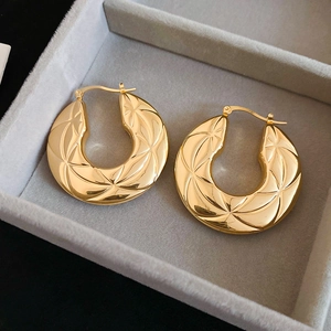 Detail view of gold hoop earrings with star geometric textured engraving in a jewelry box