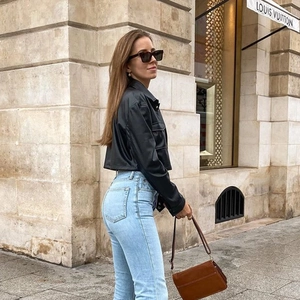 Dettaglio di una giacca corta in pelle PU nera chic con borsa a mano in pelle marrone