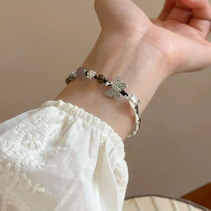 Détail d'un bracelet en perles avec pendentif papillon et anneau ondulé sur le poignet