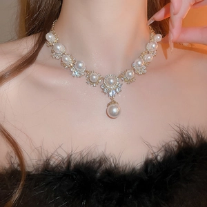Close-up of elegant gold necklace featuring round pearls and water-drop pendant on model