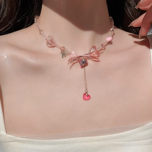 Close-up of a pink heart necklace with beaded ribbon bow worn on a model collarbone