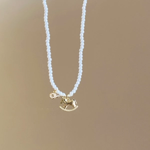 Close-up of pearl necklace with gold rocking horse pendant and crystal circle detail