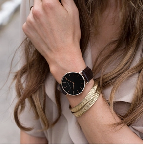 Close-up of a women's quartz watch with brown leather strap and gold engraved bracelets