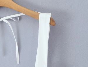 Close-up of white mini dress wide shoulder straps and thin back ties on wooden hanger