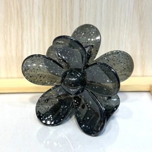Detail of a translucent black flower hair claw clip with silver glitter and metal spring