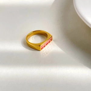 Macro view of gold signet ring with red and pink HOWDY text on white background