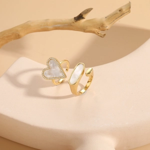 Detail of gold geometric heart and oval shell rings on minimalist stone display